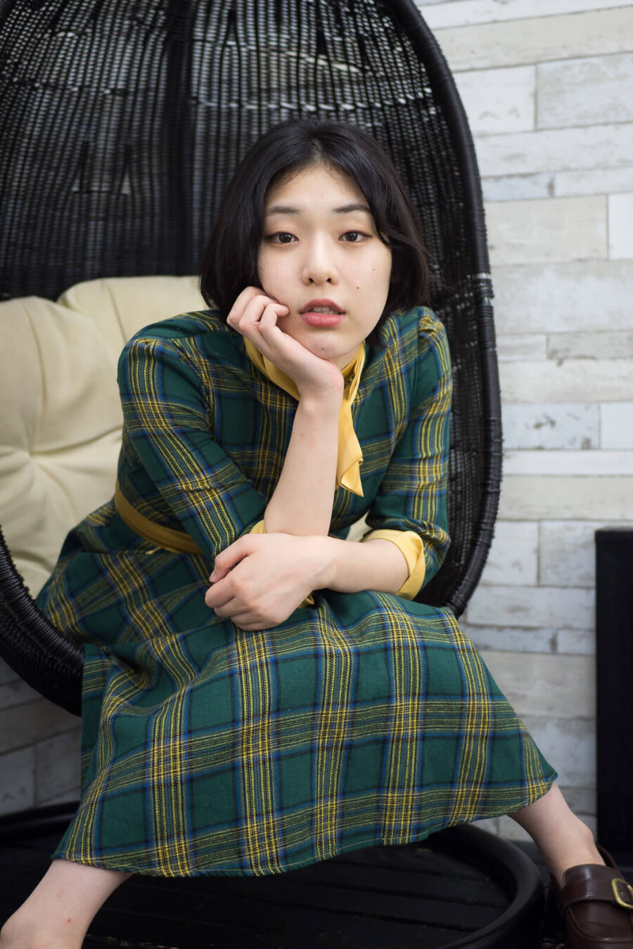 緑地に黄色いチェック柄の昭和レトロな衣装を着た女性が立て肘で腰かけている