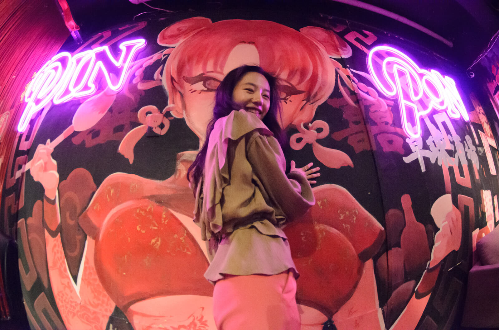 渋谷・神泉の卓球BAR「PIN PON」を借り切っての撮影時。壁に描かれたマスコットキャラクター（？）の前でポーズを取る女性。