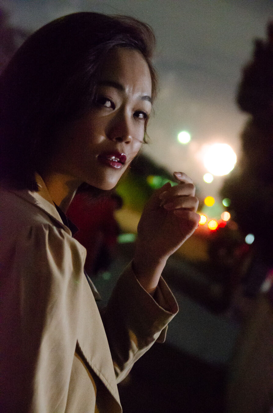 夜の道路沿い、自動車のリアライトに照らされながら振り返る女ッ製。